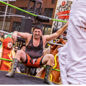 A man in camouflage-themed singlet crouches in the corner of a wrestling ring.