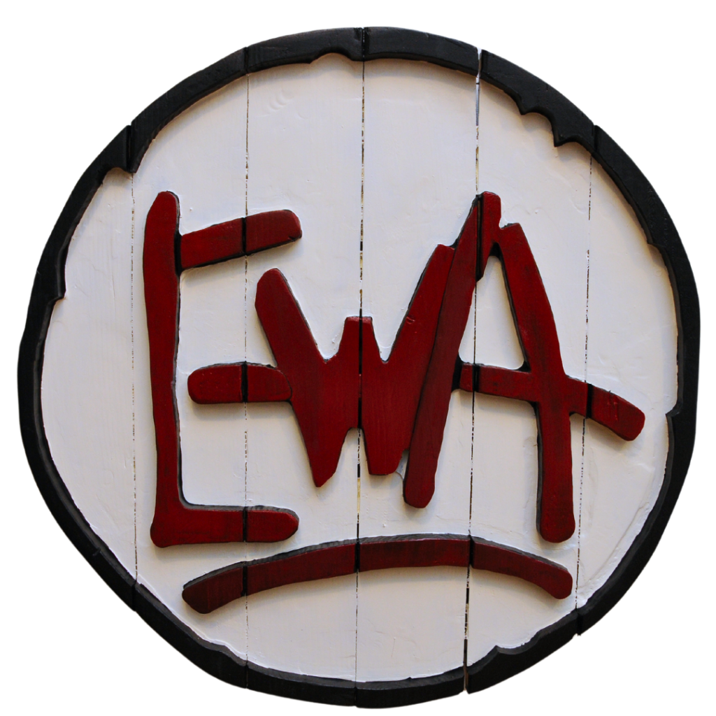 A circular, wodden logo with black trim and white vertical panels with "EWA" in red lettering overlayed.